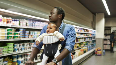 A man doing the groceries carrying a smiling baby on his chest